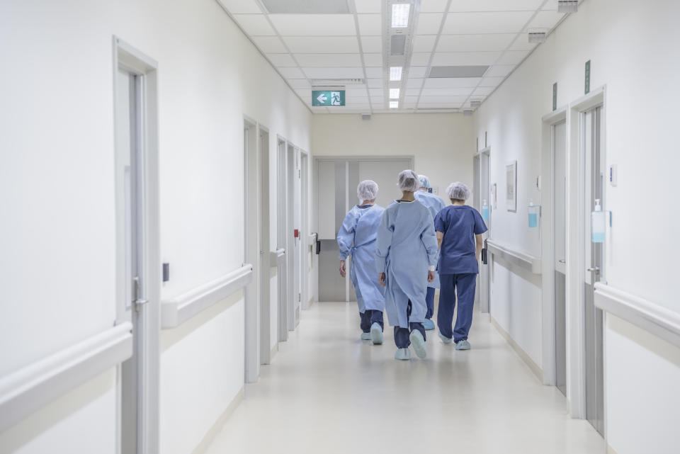 View from behind of four doctors in hospital corridor walking away from camera. Medical team in modern hospital corridor wearing surgical scrubs