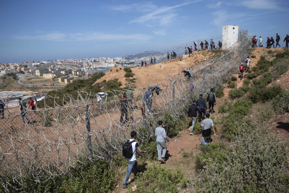 People walk past barbed wire in a forest in the Moroccan northern town of Fnideq on their way to the area at the border of Morocco and Spain, at the Spanish enclave of Ceuta, on Tuesday, May 18, 2021. About 8,000 people have streamed into the Spanish city of Ceuta from Morocco in the past two days in an unprecedented influx of migrants, most of them swimming across the border to reach the Spanish enclave in North Africa. (AP Photo/Mosa'ab Elshamy)
