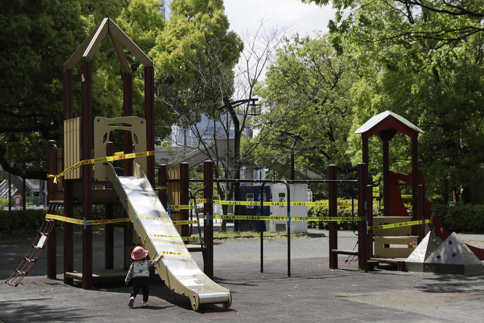 In this April 24, 2020, photo, a child walks past a slide cordoned off with ribbon reading, do not enter, in Tokyo. Under Japan's coronavirus state of emergency, people have been asked to stay home. Many are not. Some still have to commute to their jobs despite risks of infection, while others are dining out, picnicking in parks and crowding into grocery stores with scant regard for social distancing. (AP Photo/Gregorio Borgia)