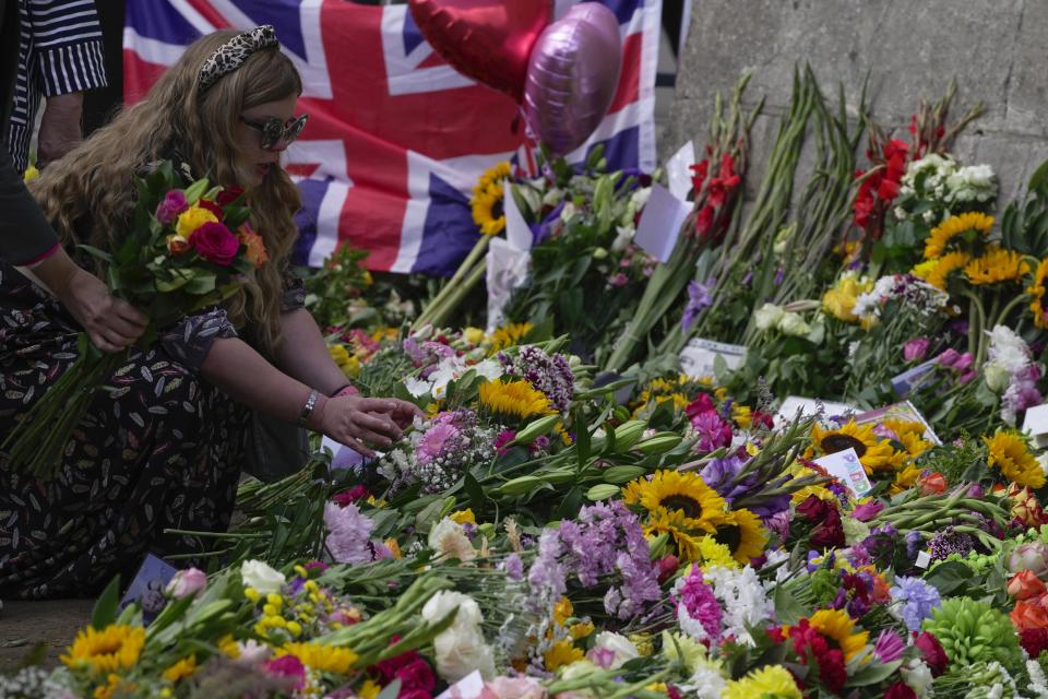 A woman places flower for the late Queen Elizabeth II outside the Windsor Castle in Windsor, England, Friday, Sept. 16, 2022. The Queen will lie in state in Westminster Hall for four full days before her funeral on Monday Sept. 19. (AP Photo/Kin Cheung)