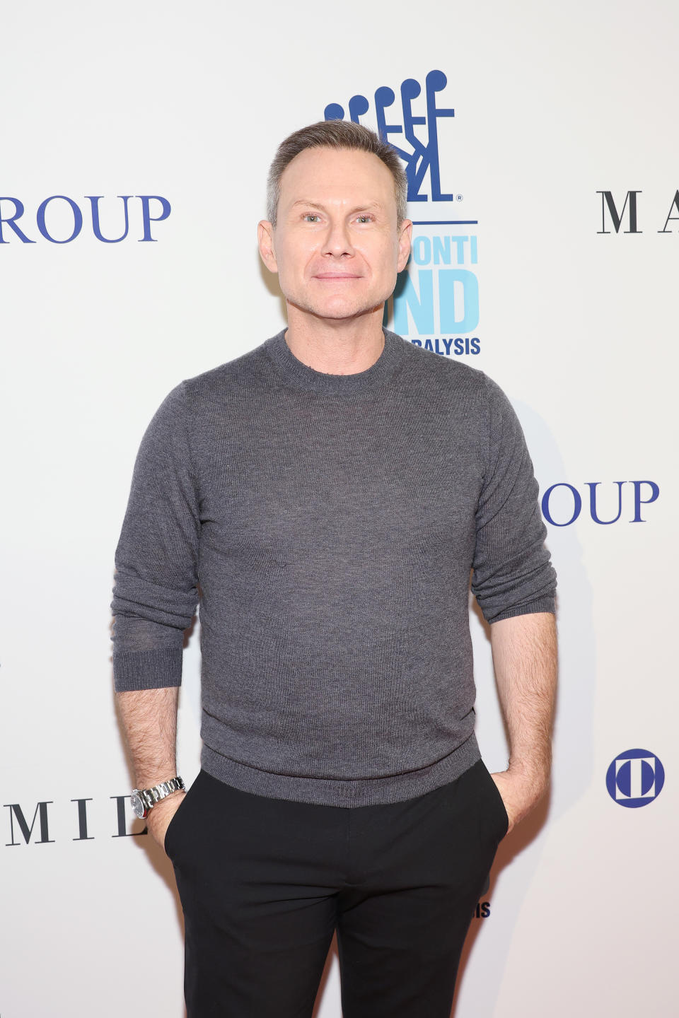 Man in a casual outfit with a sweater and black pants at a photo op event