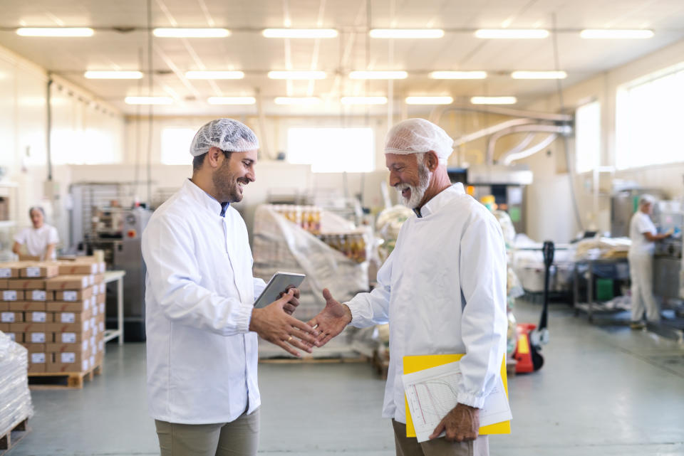 Two uniformed workers shake hands in a food manufacturing facility.