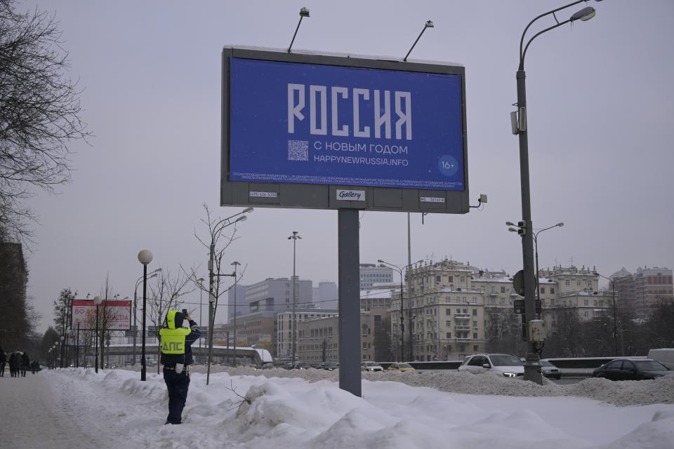 A traffic police officer takes a photo of a billboard with the words Happy New Year and the QR code in Moscow, Russia Thursday Dec. 7, 2023. Russia’s opposition have come up with a creative way of getting round censorship to call Russians to vote against President Vladimir Putin in the country’s upcoming March presidential elections — by taking out billboards under the guise of a new year greeting which leads to an anti-Putin website. (AP Photo)