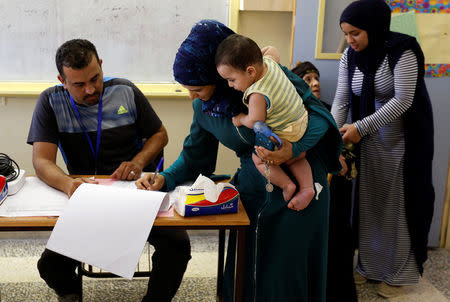 A Jordanian woman carries her son as she registers her name to cast her ballot at a polling station for parliamentary elections in Amman, Jordan September 20, 2016. REUTERS/Muhammad Hamed
