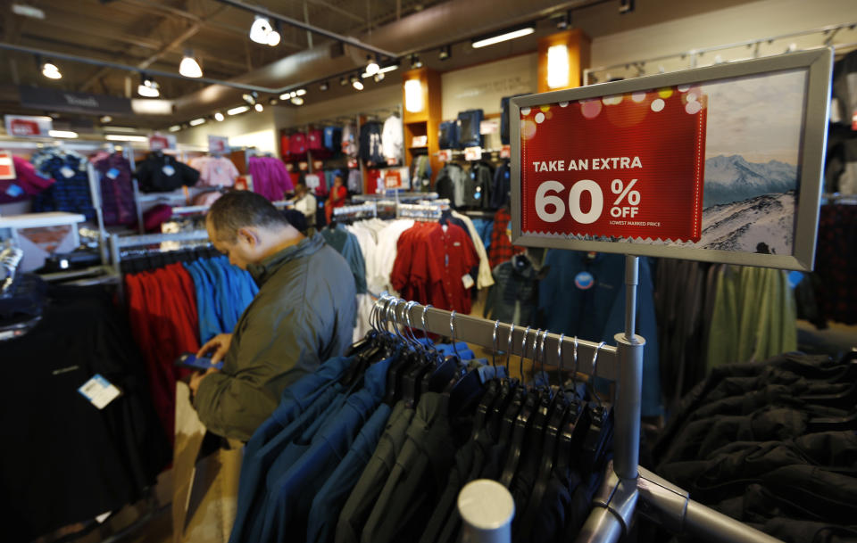 FILE - In this Dec. 24, 2018, photo a last-minute shopper scans his mobile device next to a sign marking discounts on coats at Columbia store at the Outlet Malls in Castle Rock in Castle Rock, Colo. Retailers and consumer product makers like American Textile may have received some short moment of reprieve after the Trump Administration delayed the 10% tariffs on some products which also include toys, clothing and shoes. (AP Photo/David Zalubowski, File)