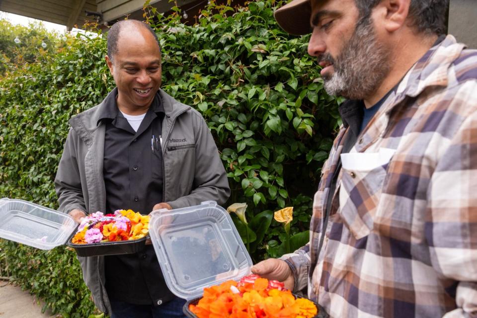 Chef Onil Chibas and Justin Dervaes hold to-go containers full of edible flowers and salad.