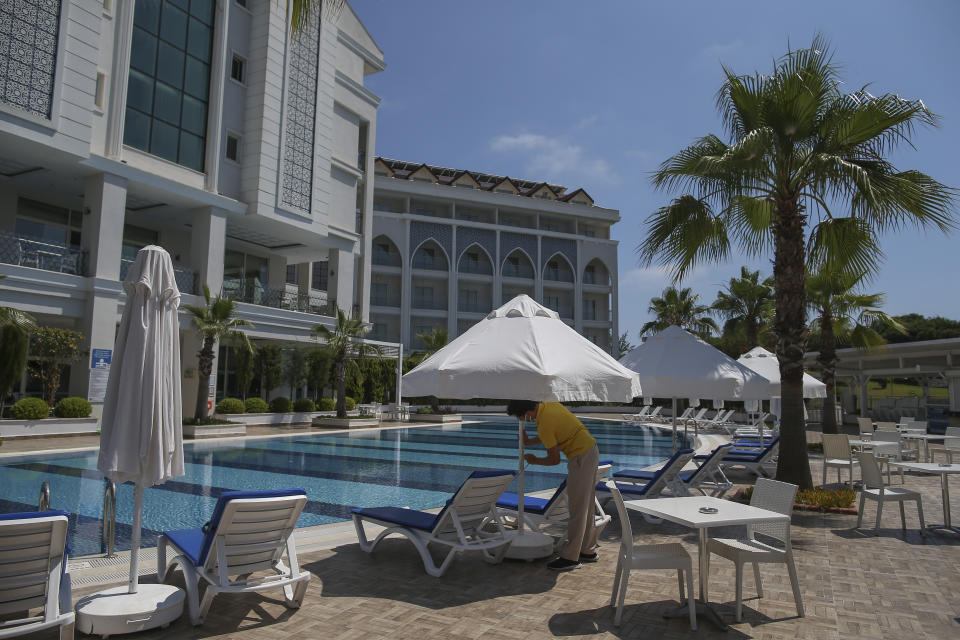 A hotel employee wearing a protective face mask opens an umbrella near a swimming pool in Antalya, southern Turkey, Saturday, June 19, 2021. Hotels in Turkey's Antalya region, a destination beloved by holidaymakers, are preparing to finally resume operations as they expect the return of international tourists after months of setbacks caused by the pandemic that halted travel. (AP Photo/Emrah Gurel)