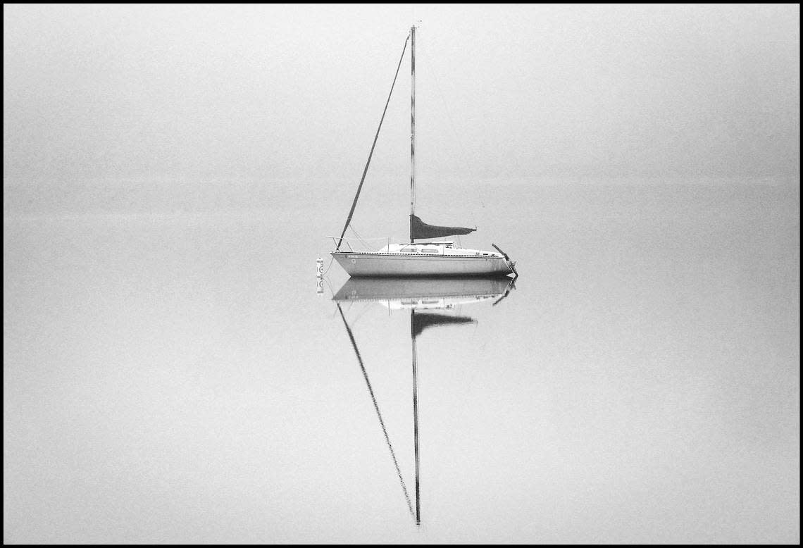 A sailboat sits in the calm fog- shrouded waters of Lake Wheeler in south Raleigh