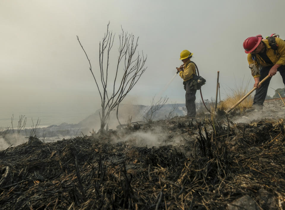 County of Santa Barbara Fire Departement firefighters extinguish a roadside fire off the U.S. 101 highway Wednesday, Oct. 13, 2021, in Goleta, Calif. A wildfire raging through Southern California coastal mountains threatened ranches and rural homes and kept a major highway shut down Wednesday as the fire-scarred state faced a new round of dry winds that raise risk of flames. (AP Photo/Ringo H.W. Chiu)