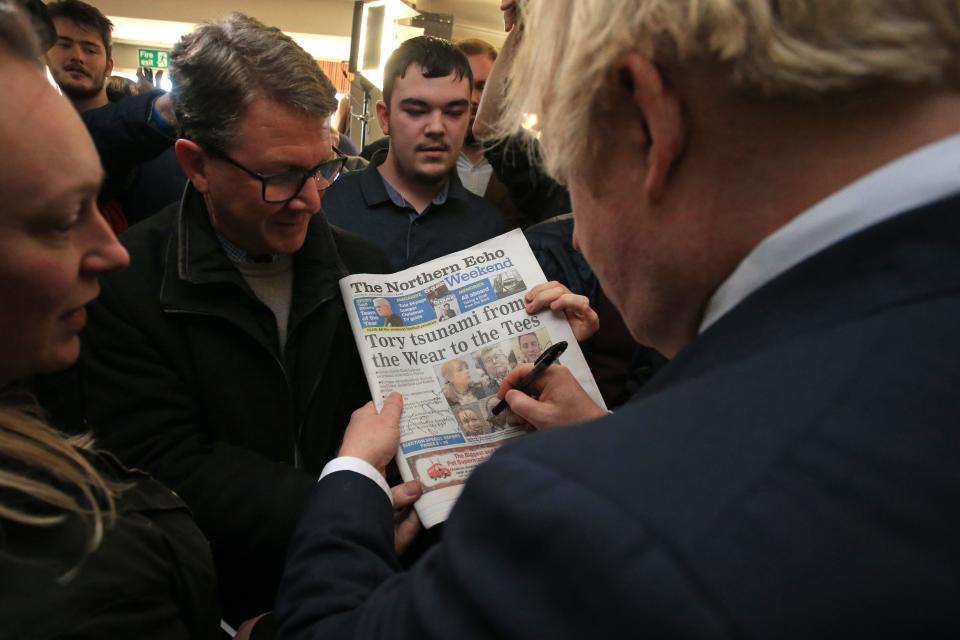 Britain's Prime Minister Boris Johnson signs a copy of The Northern Echo for a supporter during a visit to see newly elected Conservative party MP for Sedgefield, Paul Howell at Sedgefield Cricket Club in County Durham, north east England on December 14, 2019, following his Conservative party's general election victory. - Prime Minister Boris Johnson called on Britons to put years of bitter divisions over the country's EU membership behind them as he vowed to use his resounding election victory to finally deliver Brexit next month. (Photo by Lindsey Parnaby / POOL / AFP) (Photo by LINDSEY PARNABY/POOL/AFP via Getty Images)