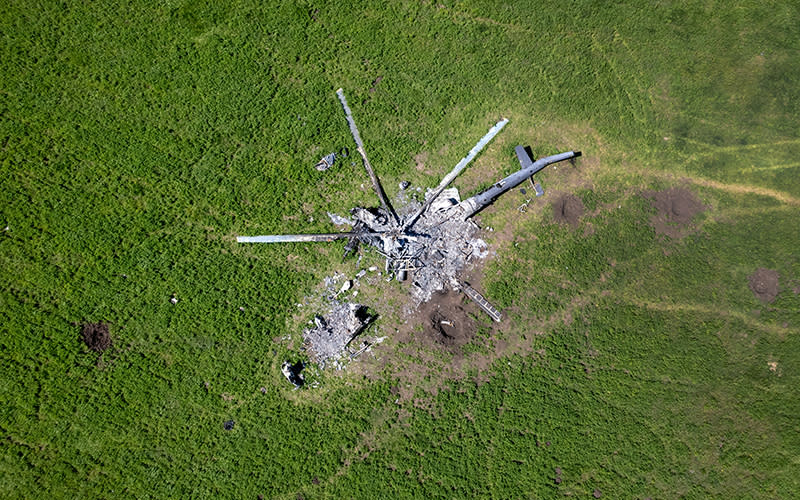 As seen from above, the remains of a Russian helicopter lie in a bomb-cratered, otherwise green field