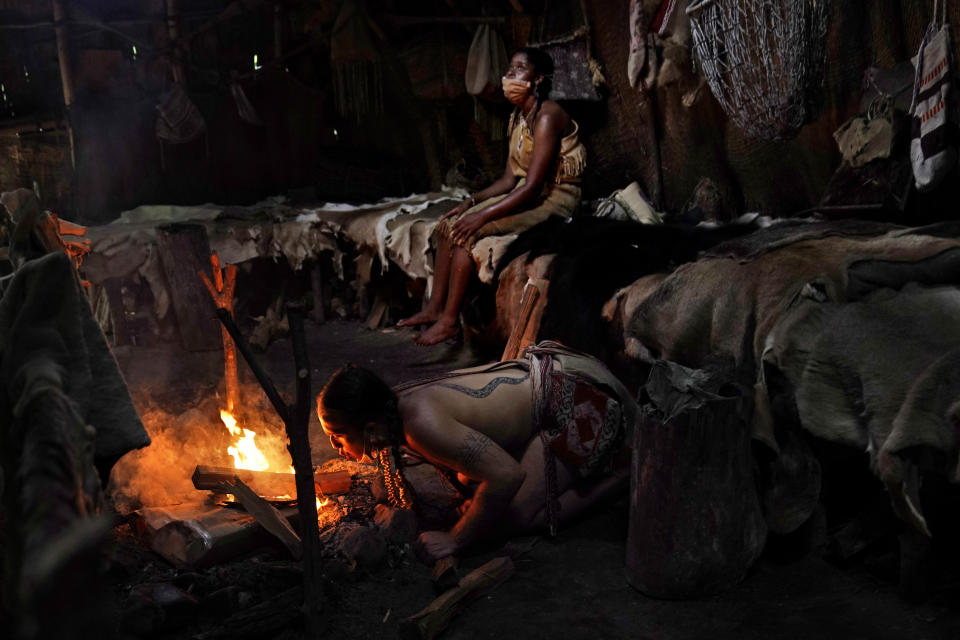 Tatanka Gibson, kneeling, a member of the Haliwa band of Nansemond and Saponi and a museum educator at Plimoth Plantation, a reconstructed living history exhibit, starts a fire inside a nush wetu after getting soaked in a downpour while waiting for visitors at the Wampanoag Homesite, Wednesday, Aug. 12, 2020, in Plymouth, Mass. (AP Photo/David Goldman)