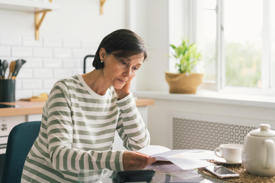 Upset female thinking about high prices while looking at utilities, gas, electricity, rental charges, water bill due to inflation and crisis. Planning personal budget while sitting in kitchen. Weighing options on how to save money