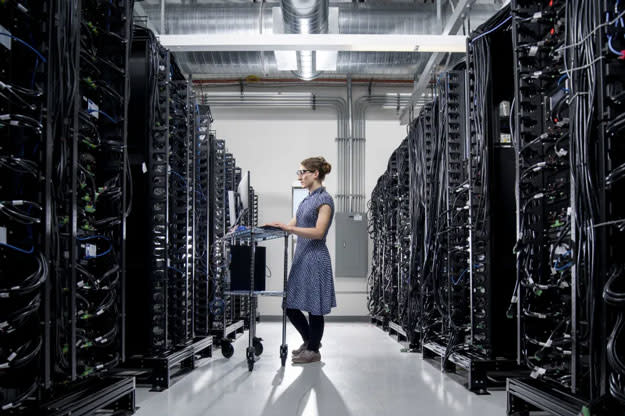 A person stands with a computer terminal in the middle of a server farm.