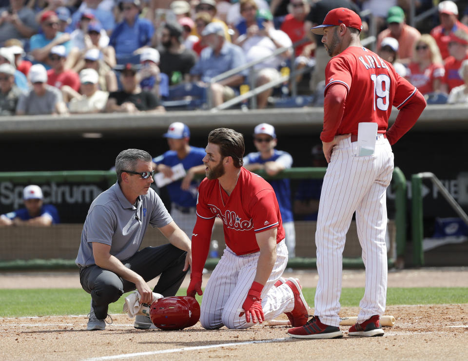 Philadelphia Phillies' Bryce Harper, center, yells toward Toronto Blue Jays pitcher Trent Thornton as manager Gabe Kapler, right, and assistant trainer Chris Mudd check on him after he was hit by a pitch during the sixth inning in a spring training baseball game, Friday, March 15, 2019, in Clearwater, Fla. Harper sustained a bruised right foot Friday, but manager Gabe Kapler said the team wasn't overly worries about the injury. Initial X-rays were negative, the team said, but Harper then left the ballpark for more detailed X-rays. (Yong Kim/The Philadelphia Inquirer via AP)