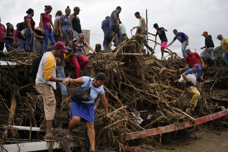 Residents cross a bridge damaged by flooding caused by a river that overflowed after days of intense rain in Las Tejerias, Venezuela, Sunday, Oct. 9, 2022. (AP Photo/Matias Delacroix)