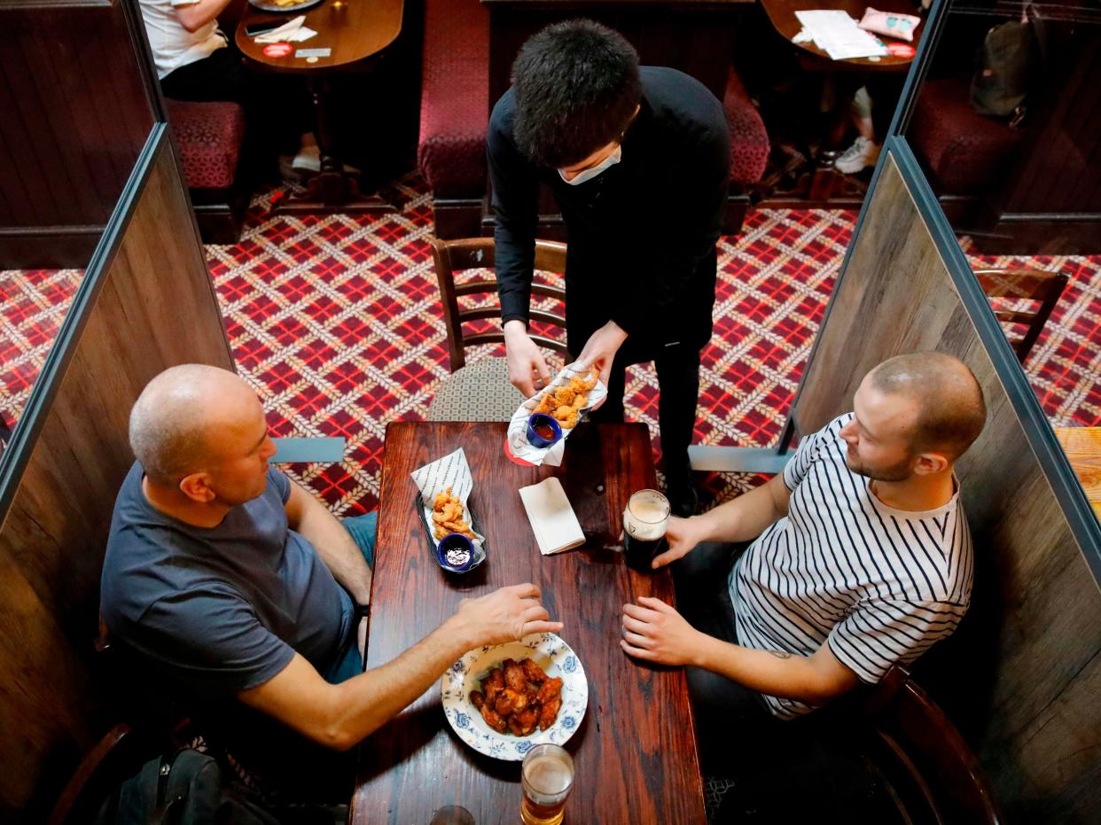 A member of bar staff wearing PPE (personal protective equipment) in the form of a face mask, serves food to seated customers inside the Wetherspoon pub (AFP via Getty Images)