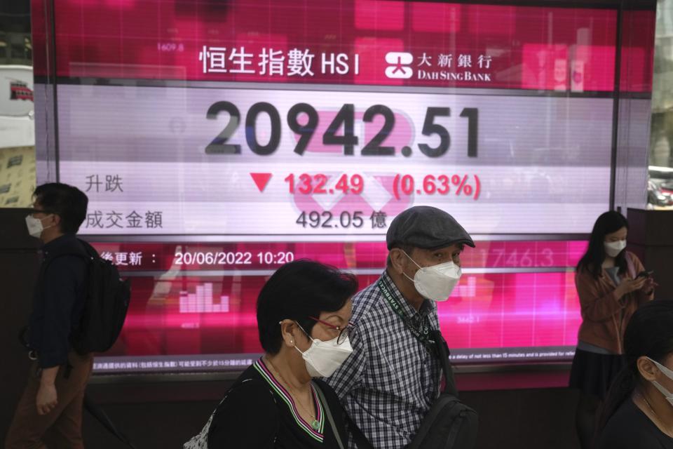 People wearing face masks walk past a bank's electronic board showing the Hong Kong share index in Hong Kong, Monday, June 20, 2022. Asian markets were mostly lower in cautious trading Monday ahead of a federal holiday in the U.S. (AP Photo/Kin Cheung)