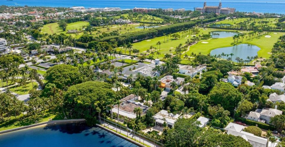 Seen at the foreground center, the main house and guesthouse at 315 Chapel Hill Road in Palm Beach stand on a lakefront site beside a massive Kapok tree that rises on the campus of the Royal Poinciana Chapel next door. The estate just changed hands for a recorded $49.6 million.