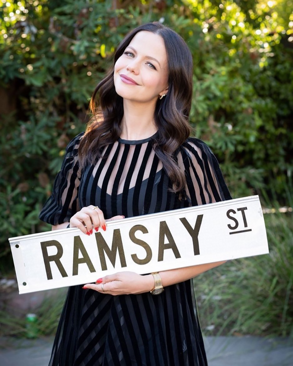 Tammin Sursok holding a Ramsay Street sign.