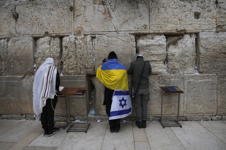 Un judío ultraortodoxo envuelto en banderas nacionales de Ucrania e Israel reza en el Muro Occidental, el lugar más sagrado donde los judíos pueden rezar en la Ciudad Vieja de Jerusalén, el viernes 4 de marzo de 2022. (AP Photo/Mahmoud Illean).