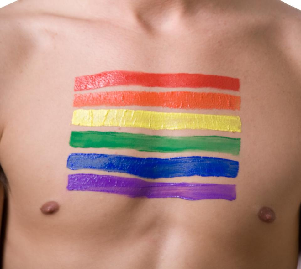 Person blowing bubble gum, chest painted with horizontal rainbow stripes symbolizing LGBT pride