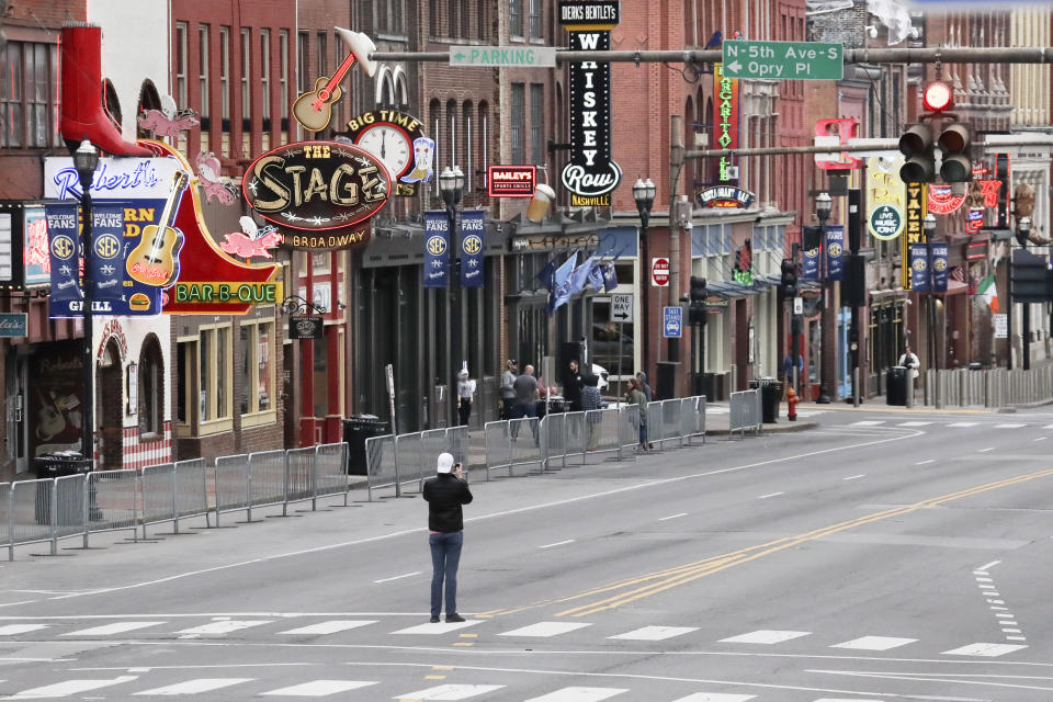 FILE - In this March 23, 2020, file photo, a man stands in the middle of Broadway to take a photo where the streets and sidewalks are normally filled in Nashville, Tenn. Many Nashville musicians have been without steady work for more than five weeks since the city shut down its clubs to slow the spread of the coronavirus. (AP Photo/Mark Humphrey, File)