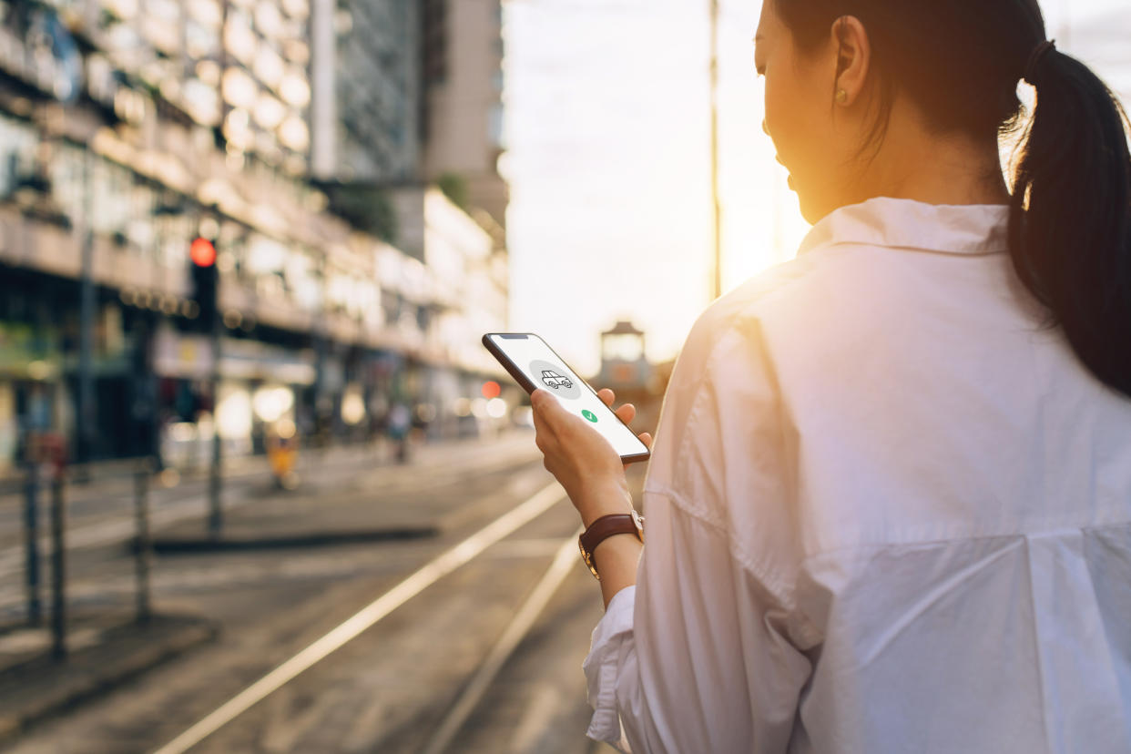 Young woman using mobile app on smartphone to arrange transportation ride in city street at sunset