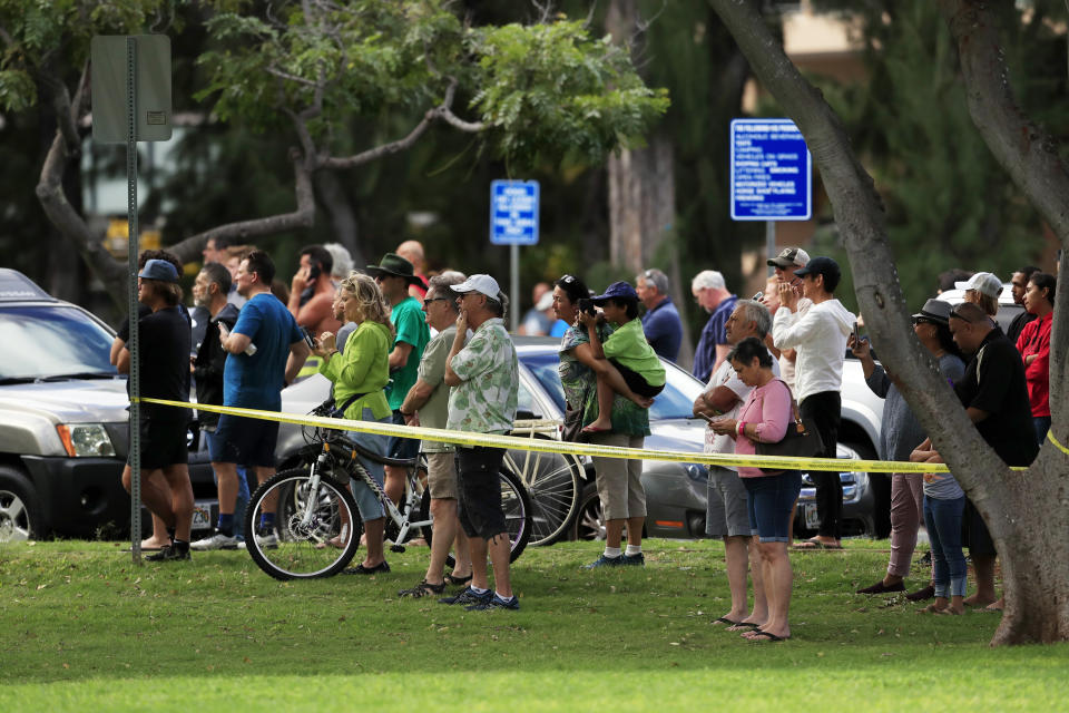 Bystanders look on after a shooting and domestic incident at a residence on Hibiscus Road near Diamond Head on Sunday, Jan. 19, 2020, in Honolulu. Witnesses say at least two Honolulu police officers were shot and two civilians were injured. Moments after the shooting, the house was set on fire, possibly by the suspect. (Jamm Aquino/Honolulu Star-Advertiser via AP)