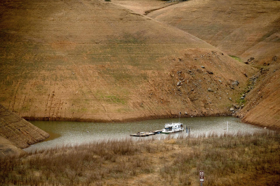 Surrounded by dry hillsides, a houseboat floats on Lake Oroville on Saturday, May 22, 2021, in Oroville, Calif. At the time of this photo, the reservoir was at 39 percent of capacity and 46 percent of its historical average. California officials say the drought gripping the U.S. West is so severe it could cause one of the state's most important reservoirs to reach historic lows by late August, closing most boat ramps and shutting down a hydroelectric power plant during the peak demand of the hottest part of the summer. (AP Photo/Noah Berger)