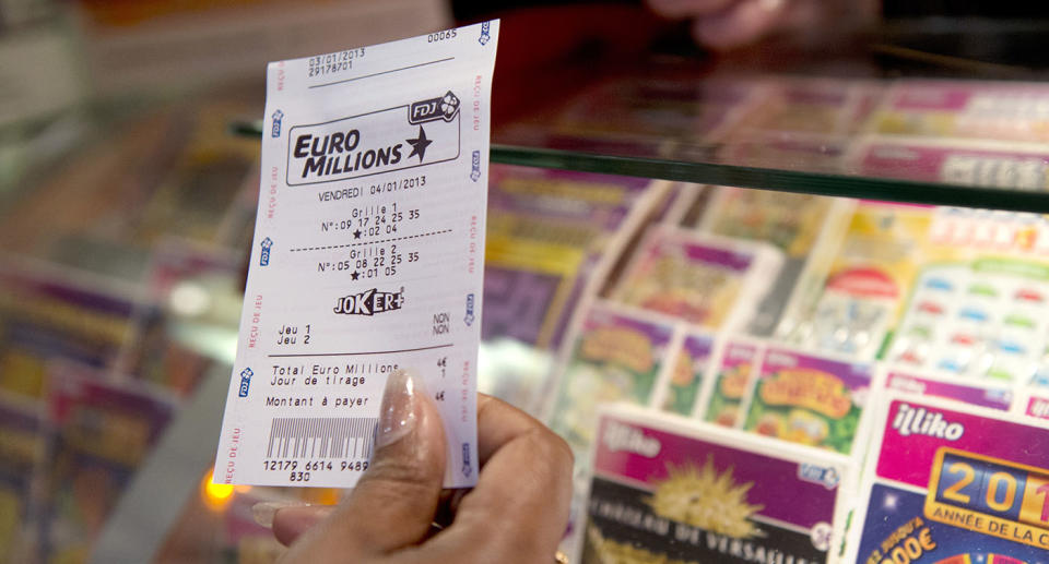 A man holds a Euromillions ticket in front of a newsagency counter.