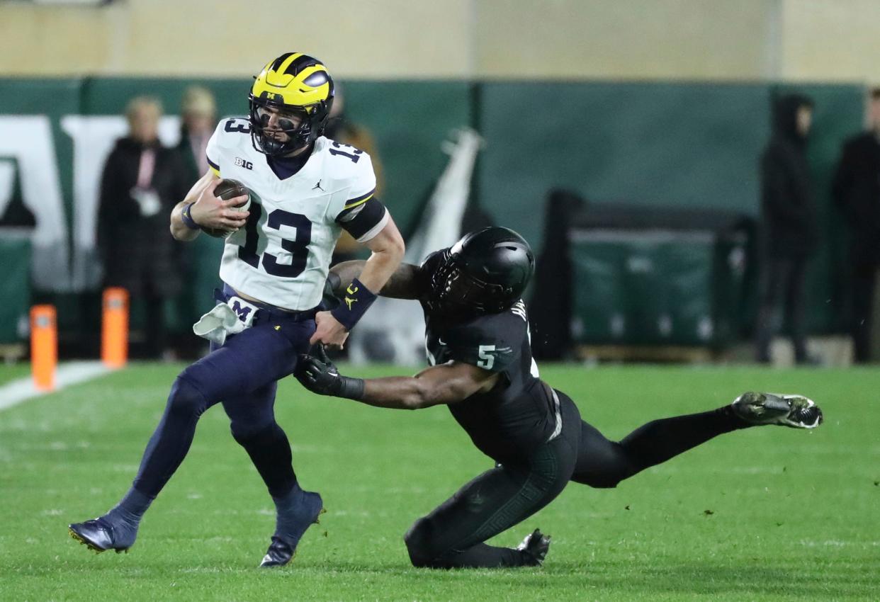 Michigan Wolverines quarterback Jack Tuttle (13) is tackled by Michigan State Spartans linebacker Jordan Hall (5) during second-half action at Spartan Stadium in East Lansing on Saturday, Oct. 21, 2023.