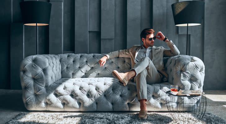 Handsome stylish man in beige suit at home sitting on sofa; luxury goods and experience stocks. global stocks to buy