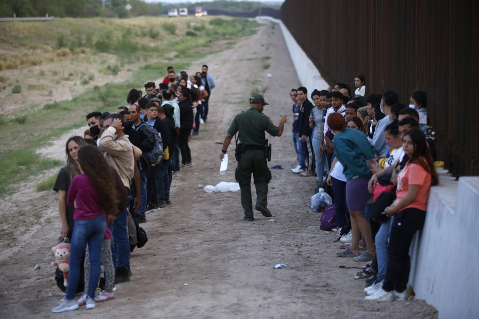 FILE - A group of migrants stand next to the border wall as a Border Patrol agent takes a head count in Eagle Pass, Texas, Saturday, May 21, 2022. The Eagle Pass area has become increasingly a popular crossing corridor for migrants, especially those from outside Mexico and Central America, under Title 42 authority, which expels migrants without a chance to seek asylum on grounds of preventing the spread of COVID-19. (AP Photo/Dario Lopez-Mills, File)