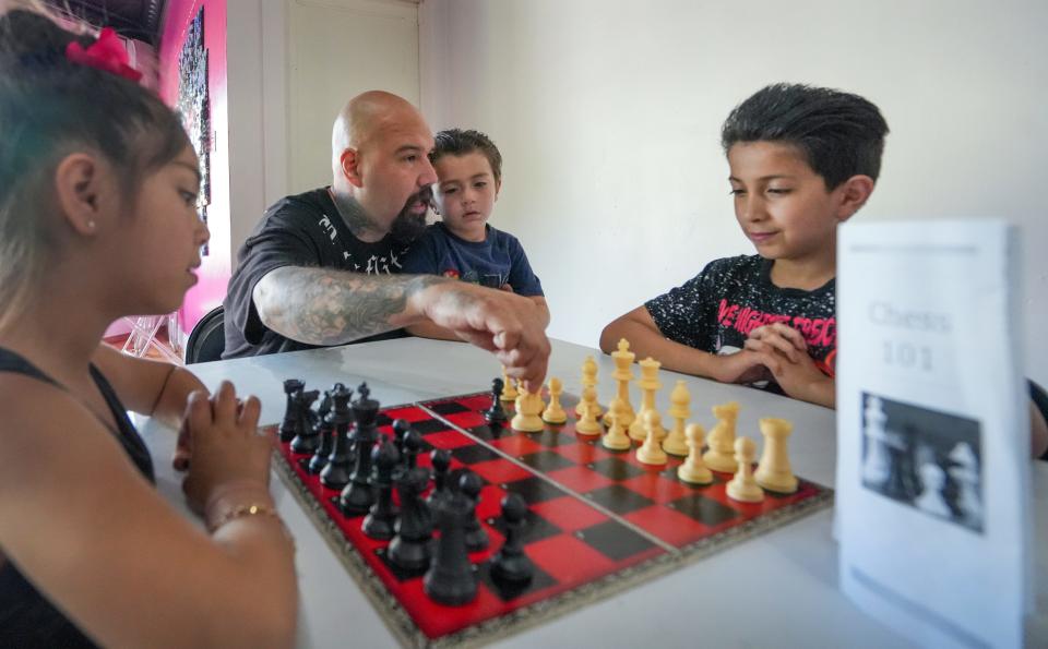 Eric Ramos holds his 4-year-old son Santino while he shows his children Victor,9, and Eva,7, that the knight moves in an "L" shape during Hip Hop Chess Club put on by "Your Move MKE" Friday, June 17, 2022, at 2926 West Forest Home Ave., Milwaukee. Hip Hop Chess Club meets every third Friday of the month.