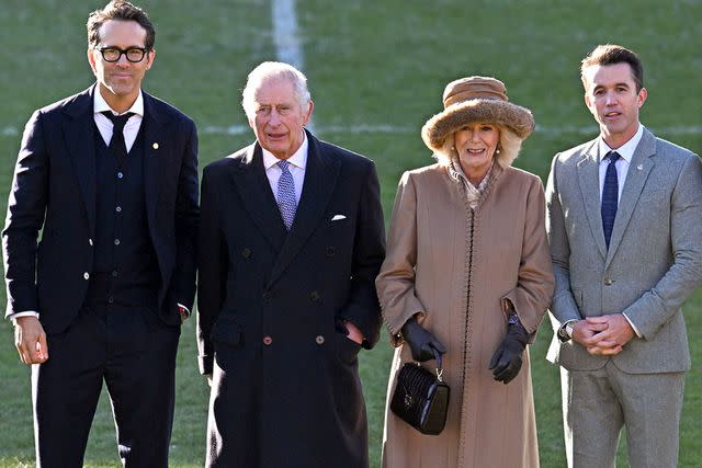 OLI SCARFF/AFP via Getty King Charles and Queen Camilla with Ryan Reynolds (far left) and Rob McElhenney (far right) at Wrexham Association Football Club's Racecourse Ground in December 2022.