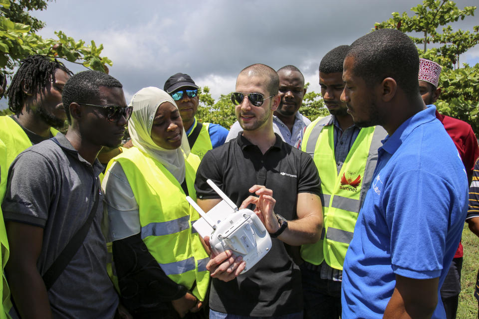 In this photo taken Thursday, Oct. 31, 2019, Eduardo Rodriguez, center, of drone manufacturer DJI, shows trainee drone pilots from the State University of Zanzibar how to fly a drone to spray the breeding grounds of malaria-carrying mosquitoes, at Cheju paddy farms in the southern Cheju region of the island of Zanzibar, Tanzania. Drones spraying a silicone-based liquid that spreads across the large expanses of stagnant water where malaria-carrying mosquitoes lay their eggs, are being tested to help fight the disease on the island of Zanzibar, off the coast of Tanzania. (AP Photo/Haroub Hussein)