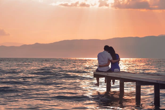 A couple sitting on a dock overlooking a lake watching the sun set