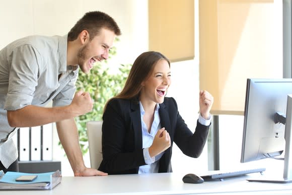 A man and woman cheer as they look at a computer screen.