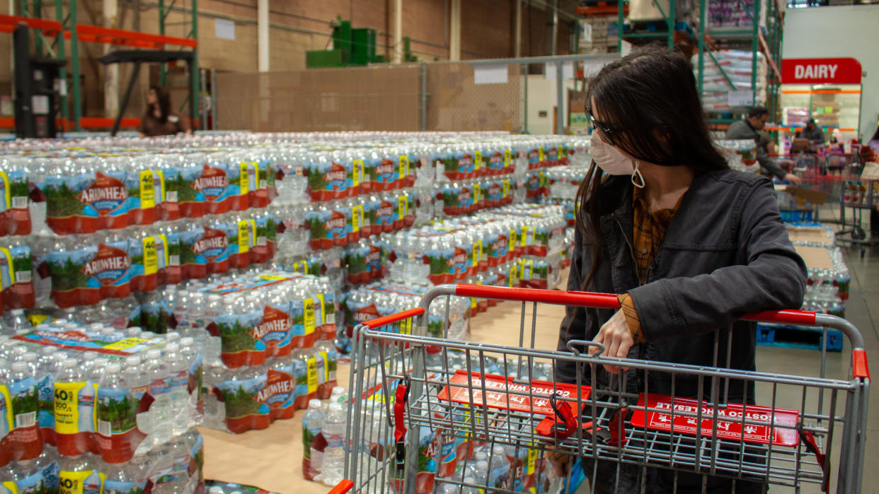 Albuquerque, New Mexico / USA - March 12 2020: Woman wearing face mask with cart shops for water bottles in grocery store amid reports of coronavirus COVID-19 cases in Albuquerque, New Mexico