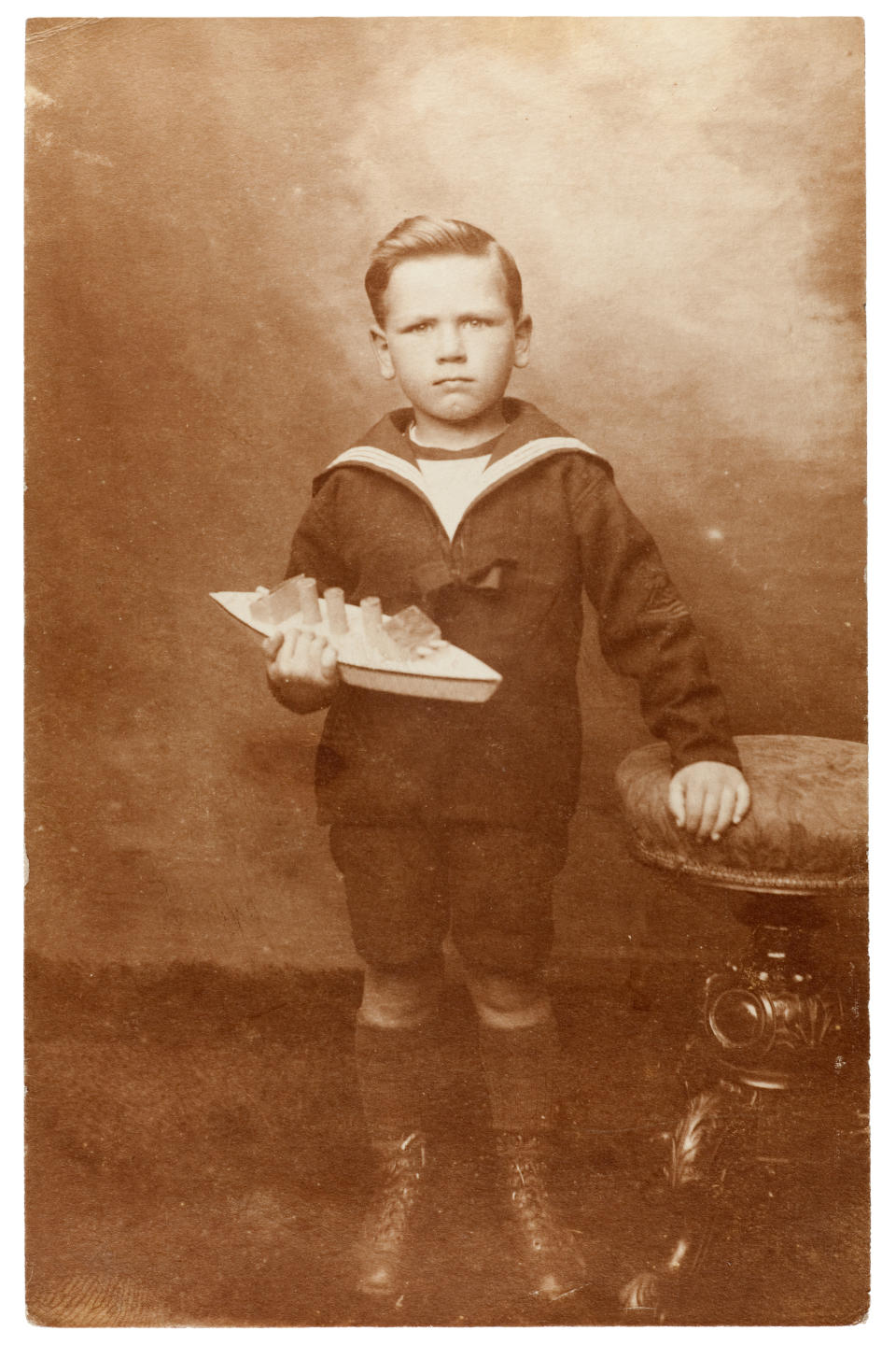 photo of a young boy in a sailor's outfit holding a toy boat, circa 1910