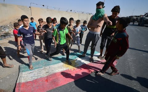 Iraqi boys walk over the Kurdish flag in Kirkuk - Credit: Stringer/Reuters