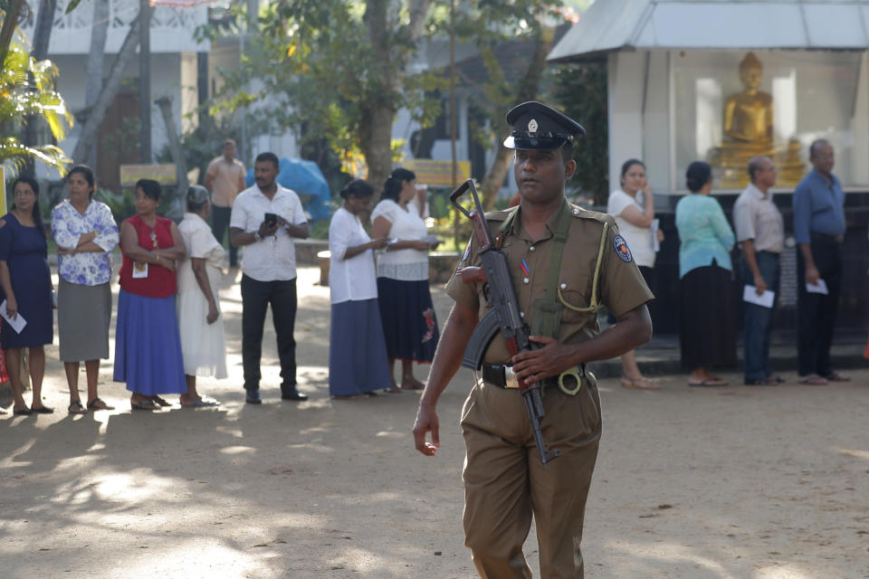 Sri Lankans queue to cast their votes as a police officer secures at a polling station during the presidential election in Colombo, Sri Lanka, Saturday, Nov. 16, 2019. Polls opened in Sri Lanka’s presidential election Saturday after weeks of campaigning that largely focused on national security and religious extremism in the backdrop of the deadly Islamic State-inspired suicide bomb attacks on Easter Sunday. (AP Photo/Eranga Jayawardena)