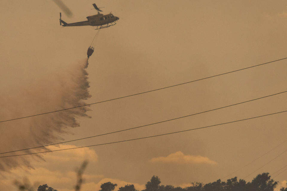 A helicopter makes a water drop over a wildfire in Estepona, Spain, Thursday, Sept. 9, 2021. Nearly 800 people have been evacuated from their homes and road traffic has been disrupted as firefighting teams and planes fight a wildfire in southwestern Spain. (AP Photo/Sergio Rodrigo)
