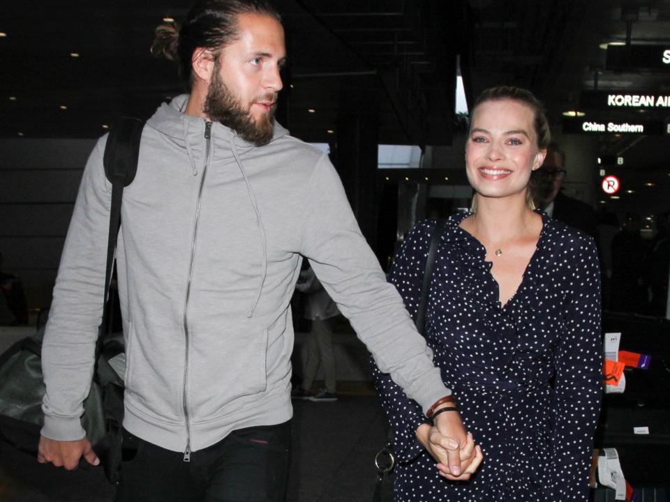 Tom Ackerley and Margot Robbie holding hands while walking through LAX in January 2017.