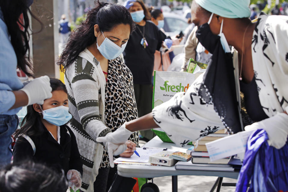 Volunteer Sequaña Williams-Hechavarria, right, instructs youngster Jade Suarez to look beneath the table for books as Jade's mother, Maria, signs up for assistance and free supplies provided by Sistas Van during the coronavirus outbreak at a busy Bushwick intersection in the Brooklyn borough of New York, Tuesday, May 19, 2020. Sistas Van was originally launched by the nonprofit Black Women's Blueprint to help survivors of sexual and reproductive violence and physical abuse. But during the coronavirus, the women's network has pivoted to delivering badly-needed resources to black and Hispanic communities, which have had some of the city's highest rates of contagion and death toll of the fast-spreading virus. (AP Photo/Kathy Willens)