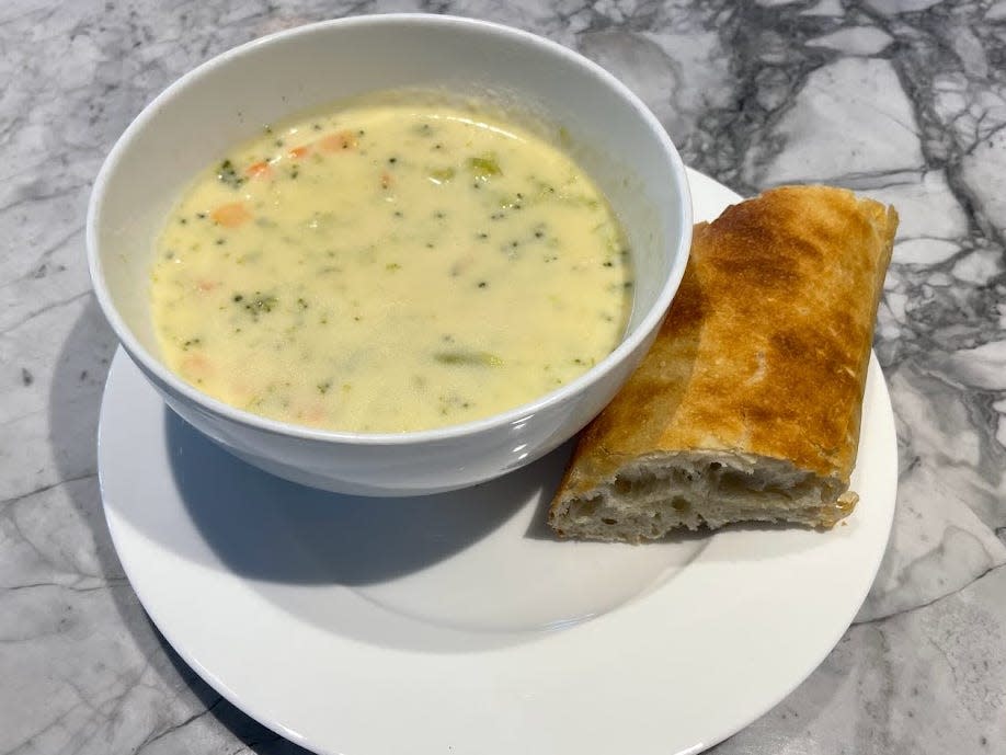 bowl of trader joes broccoli cheddar soup with a piece of bread next to it