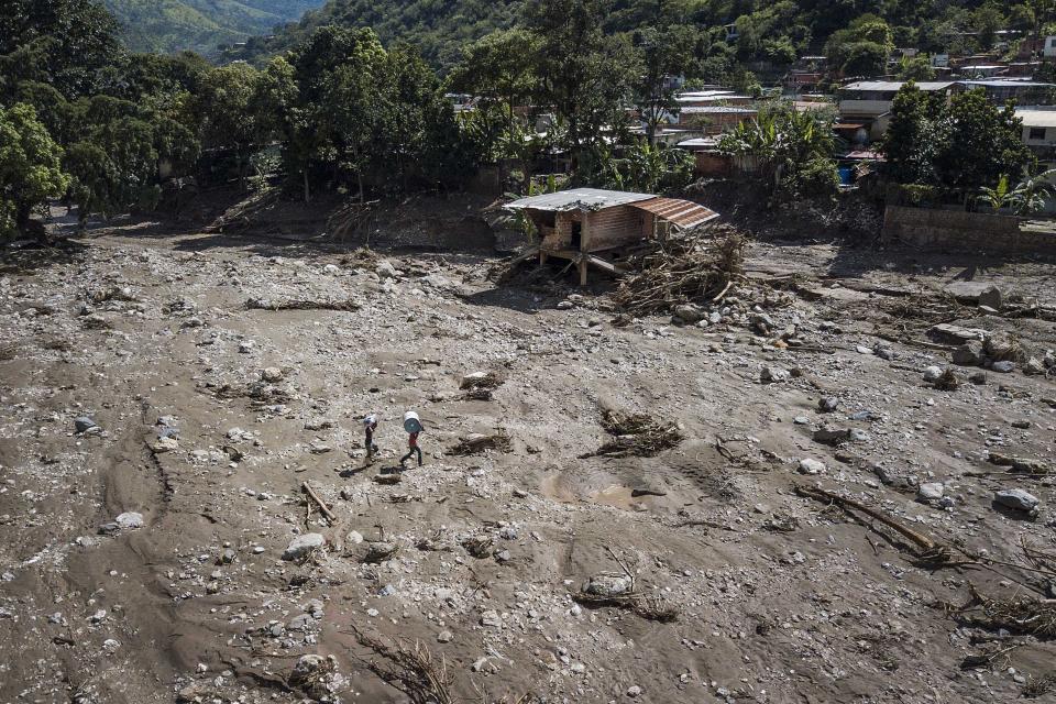 Men carry clothes and a barrel with water after a landslide and flood ripped through Las Tejerias in Venezuela, Monday, Oct. 10, 2022. The fatal landslide was fueled by days of torrential rain and floods that swept through this town in central Venezuela. (AP Photo/Matias Delacroix)