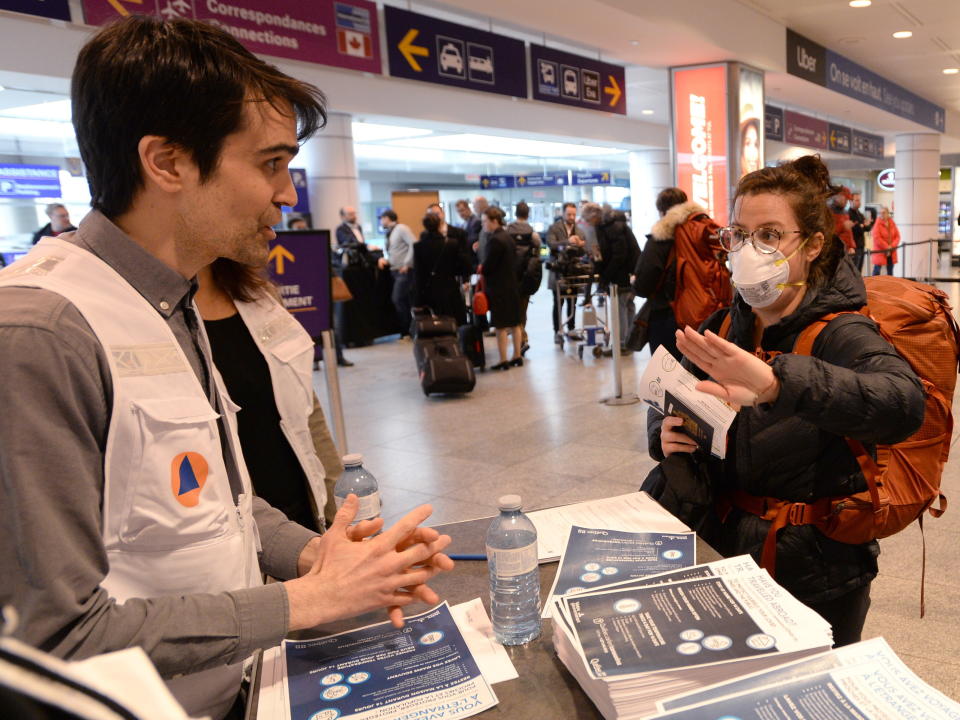 A Quebec health worker, assigned by the city of Montreal, greets a passenger and hands out information on COVID-19 at Trudeau Airport in Montreal, Monday, March 16, 2020. THE CANADIAN PRESS/ Ryan Remiorz