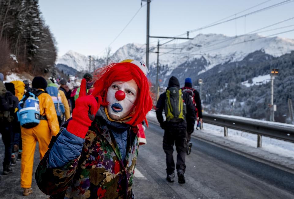 Un hombre vestido de payaso gesticula mientras marcha con otros cientos de manifestantes durante una protesta desde Landquart a Davos, pasando por la ciudad de Klosters, Suiza, el lunes 20 de enero de 2020. El Foro Económico Mundial comenzó el martes. (Foto AP/Michael Probst)